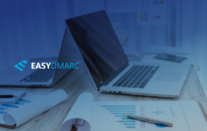 two laptops on a desk full of papers and pens,picture covered with the EasyDMARC logo