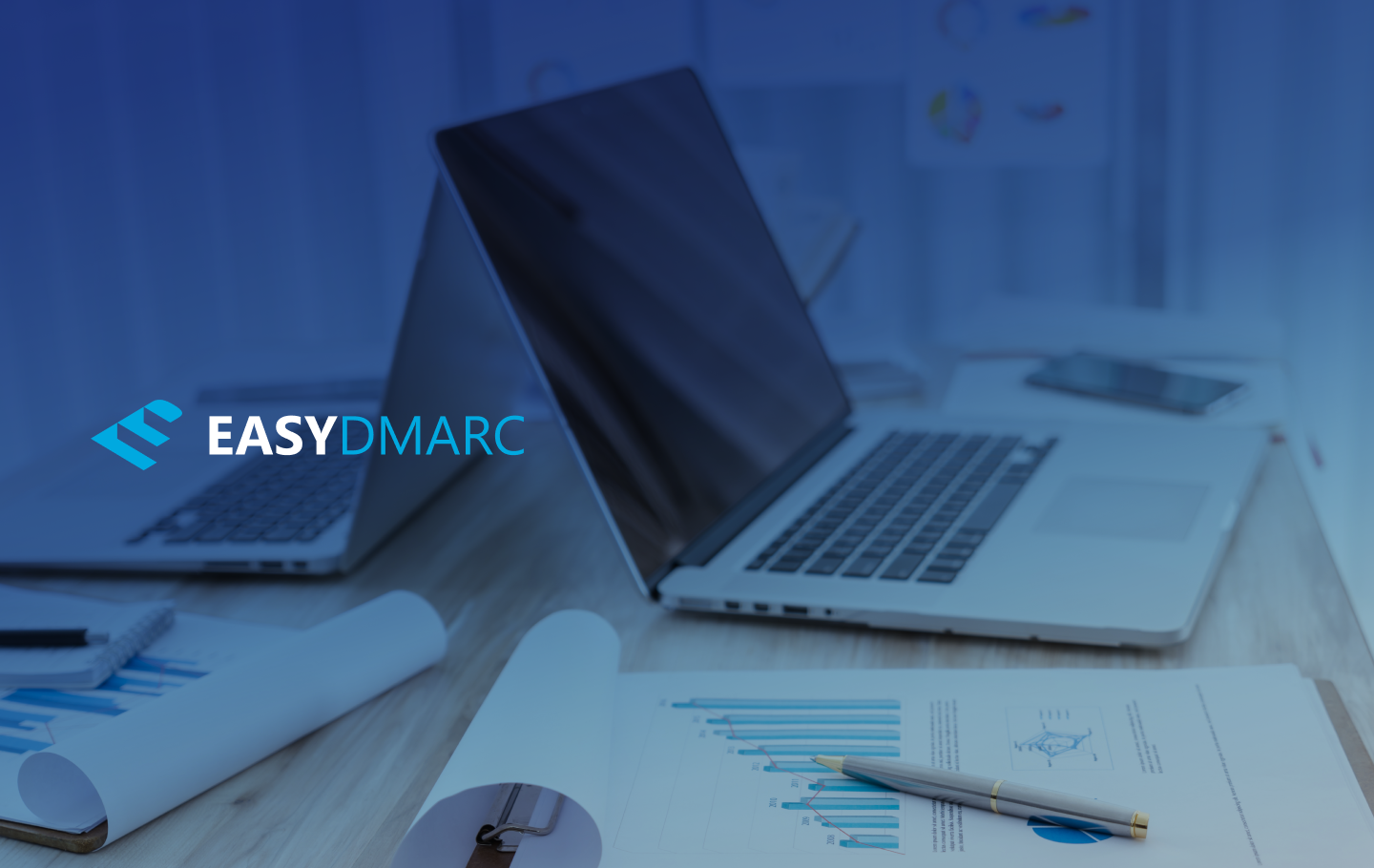 two laptops on a desk full of papers and pens,picture covered with the EasyDMARC logo